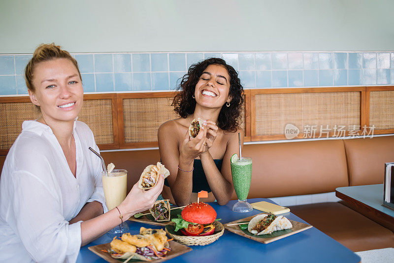 幸福多样的时髦女孩的肖像享受友好会议在拉丁自助餐厅吃辣玉米饼和西红柿汉堡，快乐的女人微笑着在小酒馆摆着tex mex食物的相机